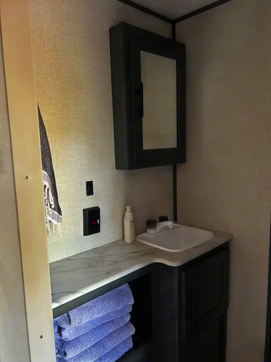 Modern compact RV rental bathroom with sink, mirror, and neatly folded towels on a marble-look countertop.. Dutchmen 3120BHS 2021