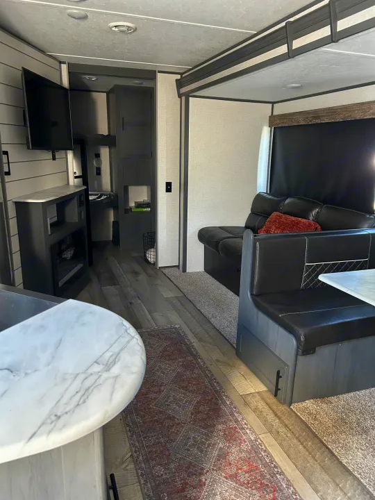 Comfortable rv rental interior showing a dinette, sofa, sleek counter, and wood-look floors with an area rug.. Dutchmen 3120BHS 2021