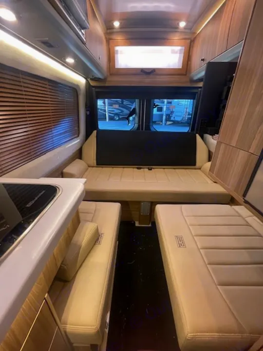 Spacious RV rental interior featuring a large convertible bed, side benches, and kitchen counter for comfortable travel.. Airstream Interstate 2023