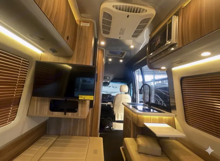 Modern RV rental interior with kitchenette, TV, microwave, and plush seating. Wood accents and bright lighting create a welcoming space.. Airstream Interstate 2023