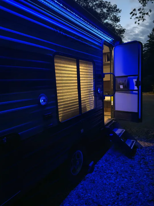 This RV rental shines at night with vibrant blue LED lights illuminating its exterior, open door, and steps, while interior light peeks from windows.. Forest River Cherokee Wolf Pup 2021