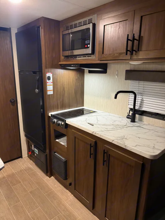Compact rv rental kitchen: black fridge, built-in microwave, two-burner stove, circular sink, and marble-look counters.. Forest River Cherokee Wolf Pup 2021