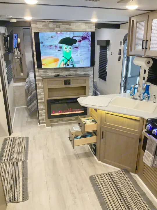 Inside this modern RV rental: a kitchen with sink, cozy electric fireplace, and TV for comfortable travels.. Keystone RV Hideout 2021