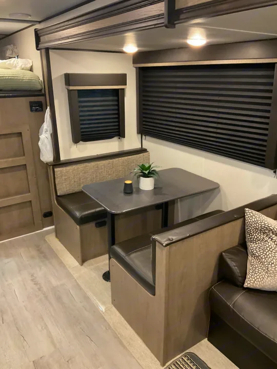 RV rental interior: A cozy dinette with dark pleated blinds, overhead lighting, and a small plant on the table.. Keystone RV Hideout 2021