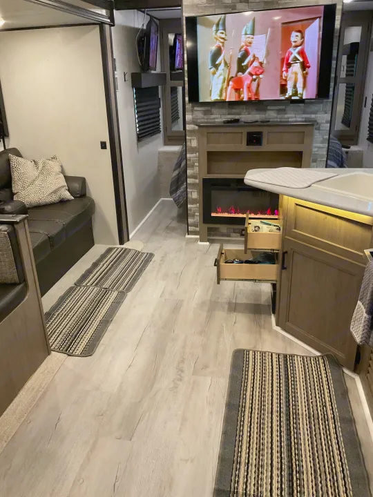RV rental: Bright RV interior showcasing a living area with a dark couch, TV over an electric fireplace, and a clean kitchen counter.. Keystone RV Hideout 2021