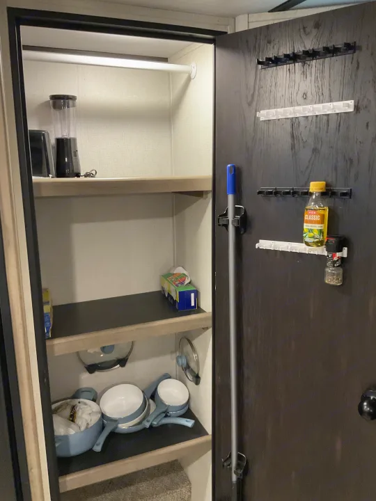 Organized RV rental pantry: shelves hold a blender, pots, tissues; door offers storage for a mop, olive oil, and spices.. Keystone RV Hideout 2021