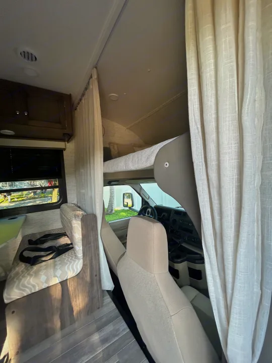 Inside an RV rental, showing the dinette, overhead bunk, and front cabin area with light-colored curtains drawn.. Entegra Ford Transit 2025