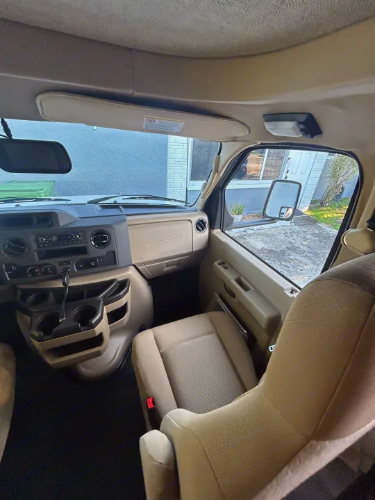 Spacious RV rental cab interior: beige dashboard, driver/passenger seats, and clear front windows. Ready for your journey!. Entegra Ford Transit 2025