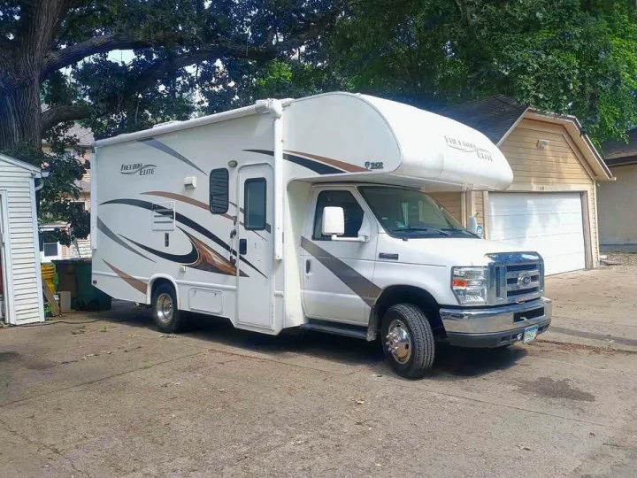 This white Thor Freedom Elite Class C **rv rental** is parked on concrete, with trees, a shed, and a garage nearby.. Thor Freedom Elite 2017