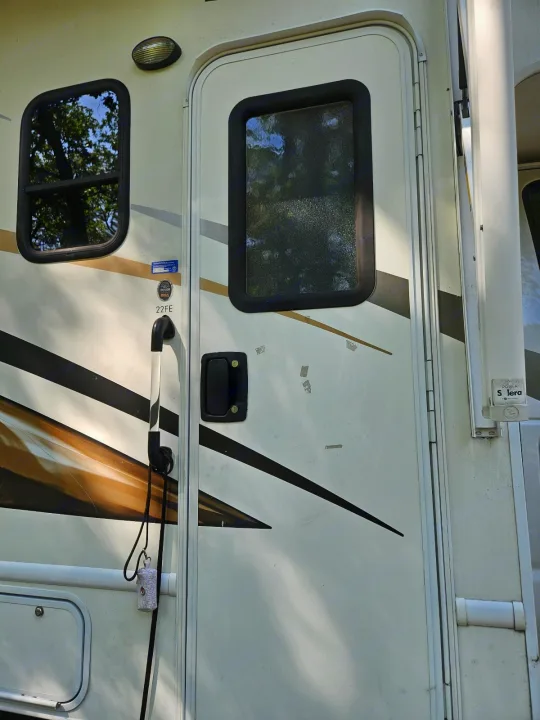 Details of an RV rental: white side, entry door, windows, exterior light & grab handle with a small bag hanging.. Thor Freedom Elite 2017