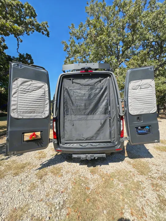 RV rental camper van with rear doors open, showing a black privacy screen and organized storage. Ready for adventure!. Winnebago Revel 2025