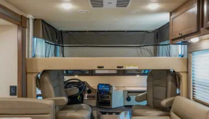 Experience an RV rental: Interior showing front cabin, driver/passenger seats, controls, and an overhead bunk with safety net.. Thor Windsport 2023
