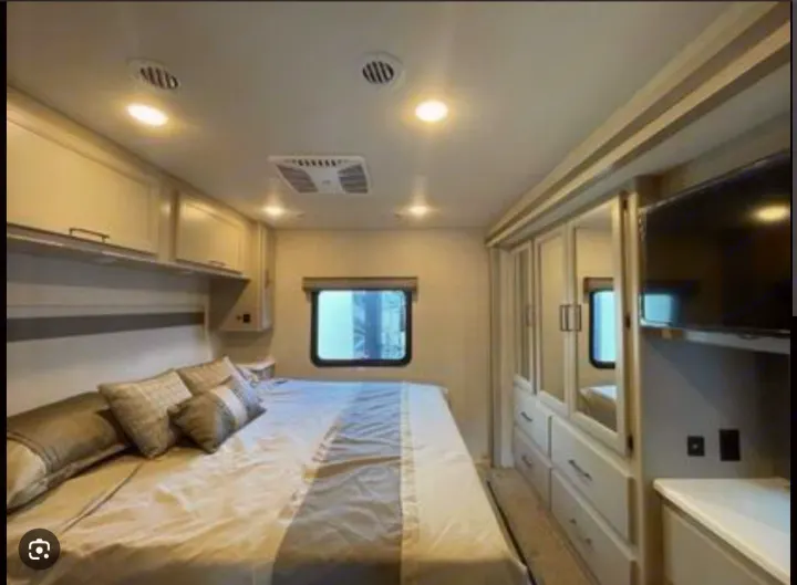 Spacious RV rental bedroom featuring a large bed, overhead storage, mirrored wardrobe, and TV, offering comfort on the road.. Thor Windsport 2023