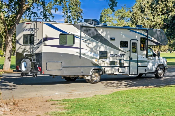 Side view of a Gulf Stream Conquest Class C rv rental motorhome, parked on pavement surrounded by trees and grass.. Gulf Stream Conquest 2023