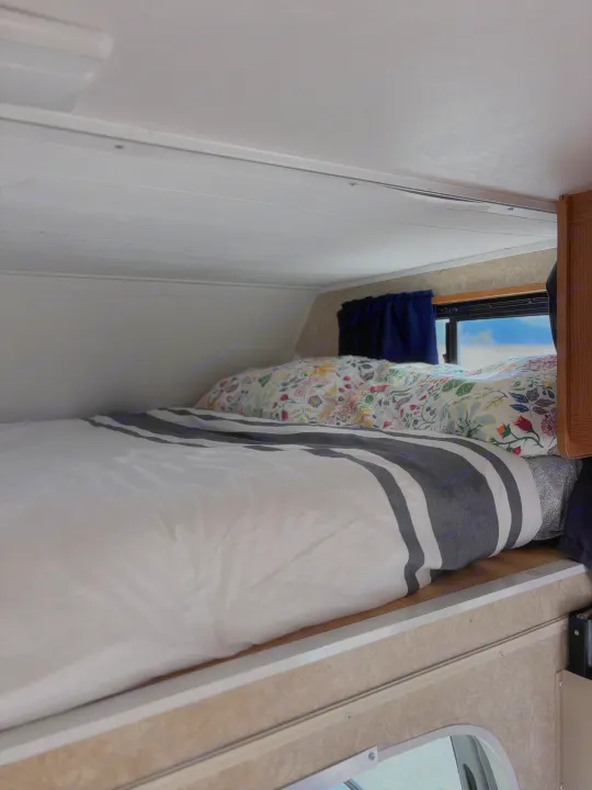 RV rental's cozy sleeping area: a striped duvet, floral pillow, and window view offer a comfortable camper bed.. Four Winds Majestic 2006