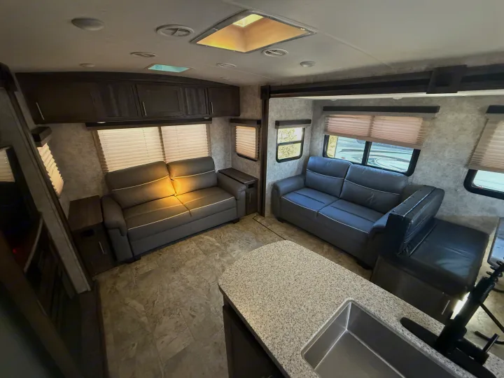 Spacious RV rental interior featuring gray sofas, a functional kitchen island with sink, and modern cabinetry.. Highland Ridge RV Light 2018