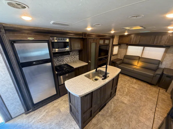 Interior of an rv rental featuring a well-equipped kitchen with an island, fridge, stove, and a cozy living room sofa.. Highland Ridge RV Light 2018
