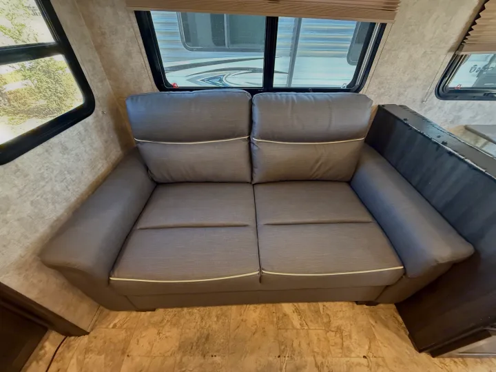 This RV rental's interior features a comfy grey sofa with white piping next to large windows, offering a bright living space.. Highland Ridge RV Light 2018