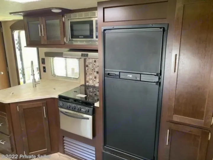 Spacious RV rental kitchen with black fridge, microwave, stovetop/oven, sink, and ample brown cabinets.. Forest River Cherokee 2018