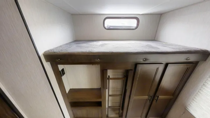Cozy RV rental bunk bed with gray mattress, small window, storage, and ladder below for a comfortable stay.. Forest River Cherokee 2018