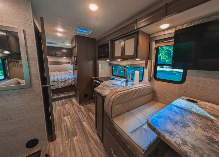 Step inside this clean, modern RV rental, featuring a full kitchen, dining booth, and a cozy bedroom just beyond.. Thor Four Winds 2021