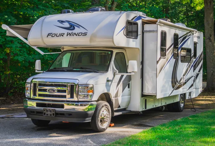 This white Four Winds Class C RV rental is set up at a sunny campsite, ideal for travel and camping adventures.. Thor Four Winds 2021