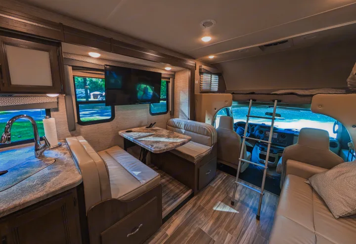 Inside a comfortable rv rental: a modern kitchen, dinette, mounted TV, and front bunk bed area with ladder.. Thor Four Winds 2021