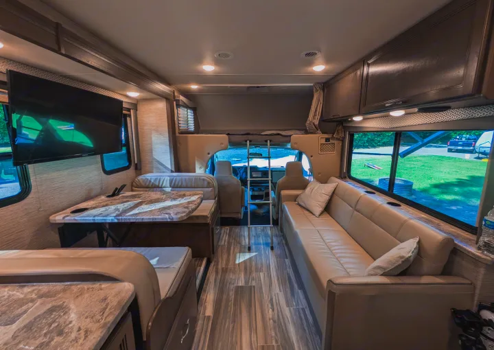 Spacious RV rental interior featuring a cozy dinette, long sofa, and overhead bunk, ideal for comfortable road trips.. Thor Four Winds 2021