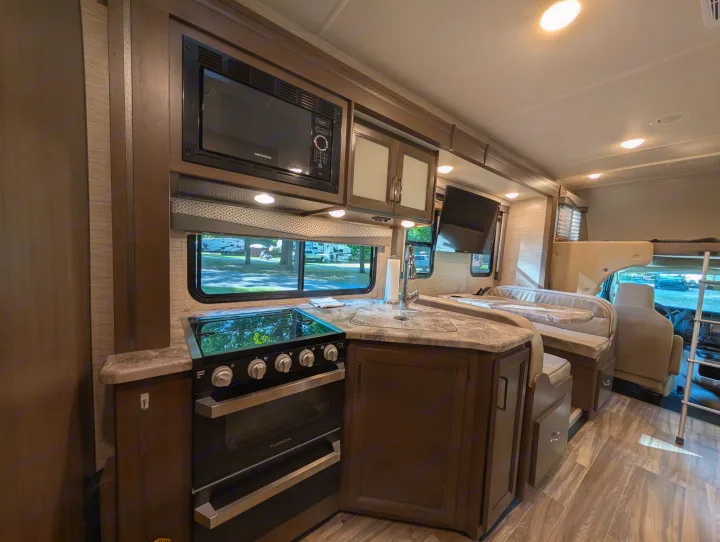 Modern RV rental kitchen and dinette with microwave, stovetop, oven, and sink, showcasing a well-equipped interior.. Thor Four Winds 2021