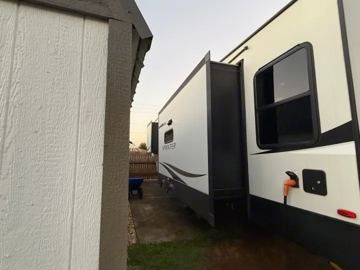 This RV rental with an extended slide-out is parked next to a building, showing its power connection and side view.. Keystone RV Sprinter Campfire 2021