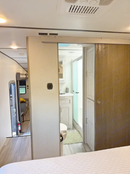 RV rental interior: bedroom foreground, bathroom with shower to the right, and hallway with bunk beds, fire extinguisher left.. Keystone RV Sprinter Campfire 2021
