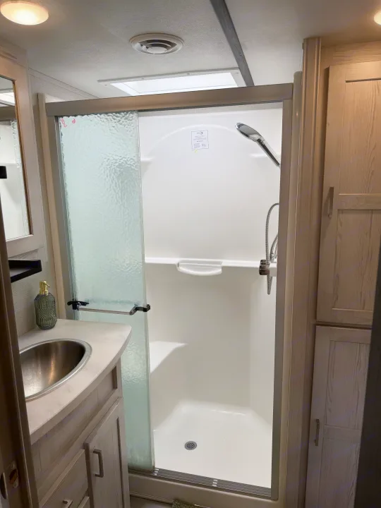 Inside an rv rental: Modern, compact bathroom featuring a bright shower with sliding glass door, a vanity with sink, and storage.. Keystone RV Sprinter Campfire 2021
