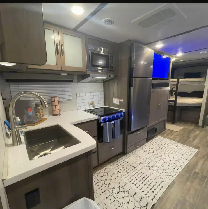This RV rental's modern kitchen and living area features a sink, stove, microwave, fridge, TV, cozy rug, and bunk beds.. Gulf Stream Envision 2023