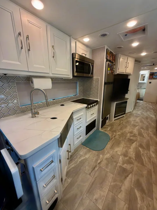 Modern rv rental kitchen featuring white cabinets, marble-look counters, a gray tile backsplash, and spacious layout.. Coachmen Encore 2022
