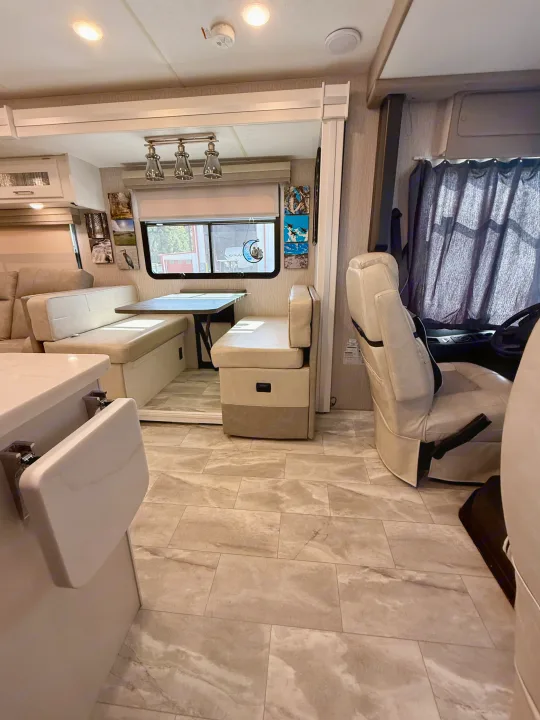 Bright RV rental interior with a spacious dinette, kitchen counter, and front seating area. Tiled floor, overhead lighting.. Coachmen Encore 2022