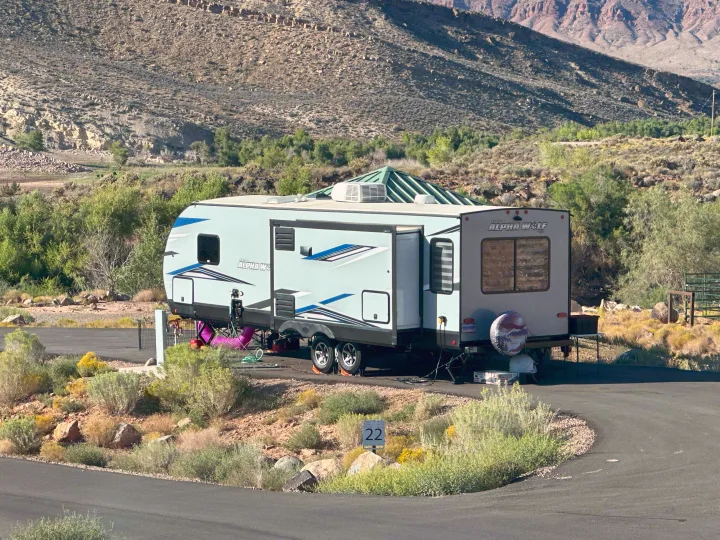 An Alpha Wolf rv rental travel trailer is ready for adventure, parked at site 22 amidst a mountain landscape and desert foliage.. Forest River Cherokee Alpha Wolf 2021