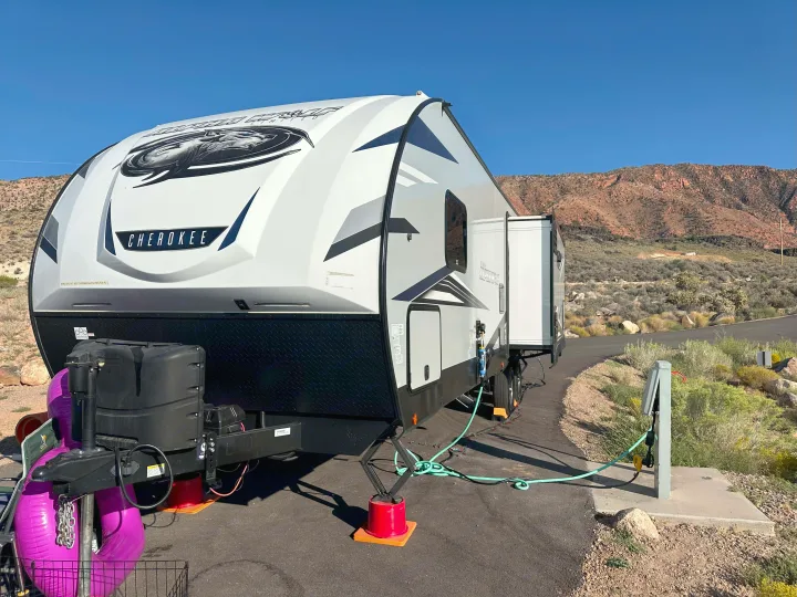 A white/gray Cherokee travel trailer RV rental, fully set up with utilities at a sunny desert campsite, mountains visible.. Forest River Cherokee Alpha Wolf 2021