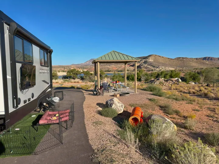 Relaxing at an RV rental site: a large RV, pets in a playpen, picnic gazebo, and scenic desert lake views under clear skies.. Forest River Cherokee Alpha Wolf 2021