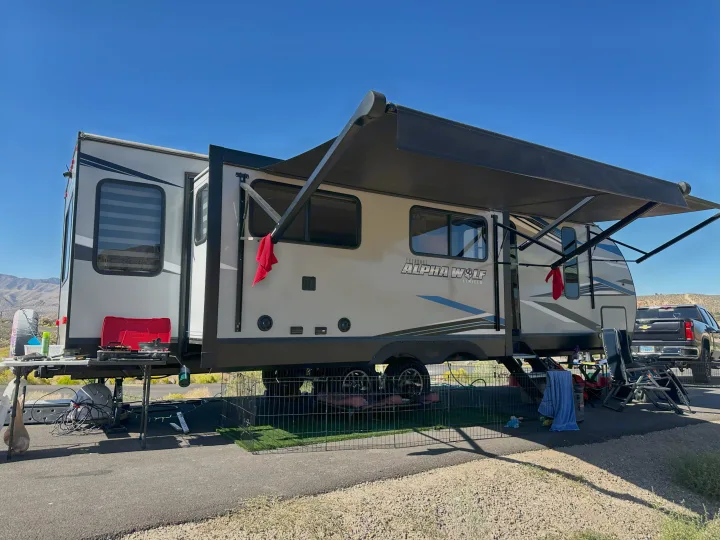 Spacious RV rental, an Alpha Wolf travel trailer, set up for camping with an outdoor kitchen, awning, and a fenced pet play area.. Forest River Cherokee Alpha Wolf 2021