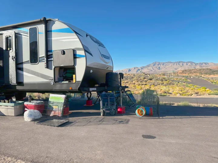 This RV rental is set up at a desert campsite, with mountain views, pet crates, and a tunnel under a clear blue sky.. Forest River Cherokee Alpha Wolf 2021