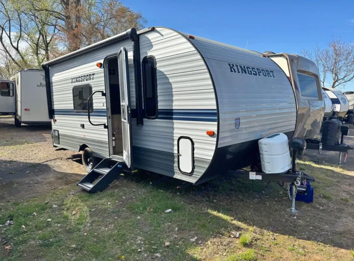This gray Kingsport travel trailer, perfect for an RV rental, is shown parked outdoors with its door open and steps down.. Gulf Stream Kingsport Super Lite 2021