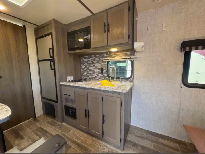 Explore this RV rental's well-equipped kitchen! Features fridge, microwave, sink, and cozy dining area. Ideal for travel.. Gulf Stream Kingsport Super Lite 2021