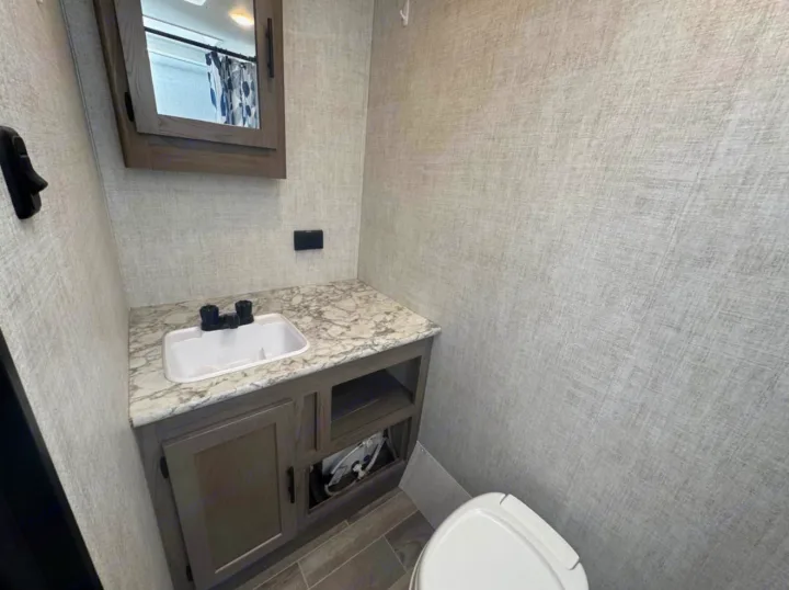 Compact RV rental bathroom with a wood-toned vanity, white sink, mirrored medicine cabinet, and toilet.. Gulf Stream Kingsport Super Lite 2021