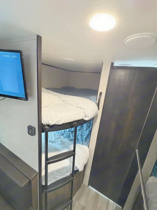 Comfortable RV rental interior with stacked bunk beds, a ladder, TV, and bright ceiling lights.. Jayco Jay Flight SLX 2024