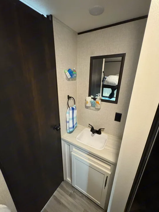 Compact RV rental bathroom with a sink, mirror, toiletries, and towel. Ideal for travel trailer stays.. Jayco Jay Flight SLX 2024