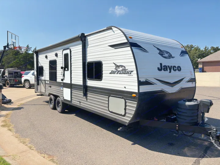 A white and grey Jayco travel trailer, ideal for rv rental, parked on a sunny day. Features an awning and dual axles.. Jayco Jay Flight SLX 2024