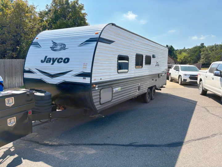 A white and gray Jayco travel trailer, a great option for an rv rental, is parked on asphalt under a clear blue sky with green trees.. Jayco Jay Flight SLX 2024