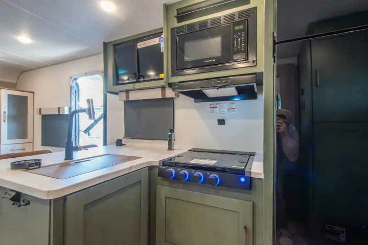 This modern RV rental kitchen features a sink, gas stove, microwave, and TV. Green cabinetry and sleek design for travelers.. Forest River No Boundaries 2026