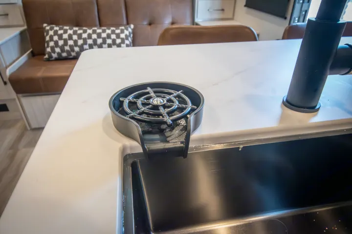 Sleek RV rental kitchen features a black sink, modern faucet, and glass rinser on a white countertop, with a cozy banquette.. Forest River No Boundaries 2026