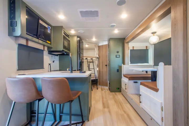 Modern RV rental interior featuring a kitchen with bar seating, a cozy dining booth, and bunk beds visible in the background.. Forest River No Boundaries 2026